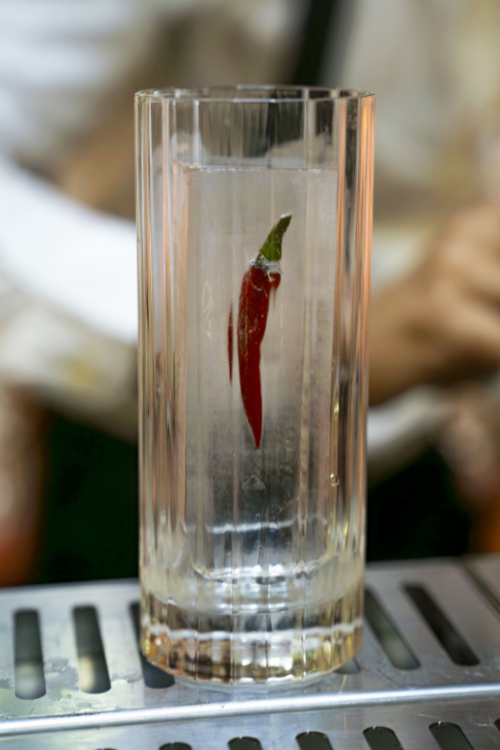 Barman devant un bar extérieur en bois avec un cocktail et des ustensiles en cuivre.