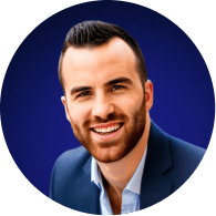 Smiling man with short dark hair and beard wearing a dark blazer over a light blue shirt against a blue circular background.