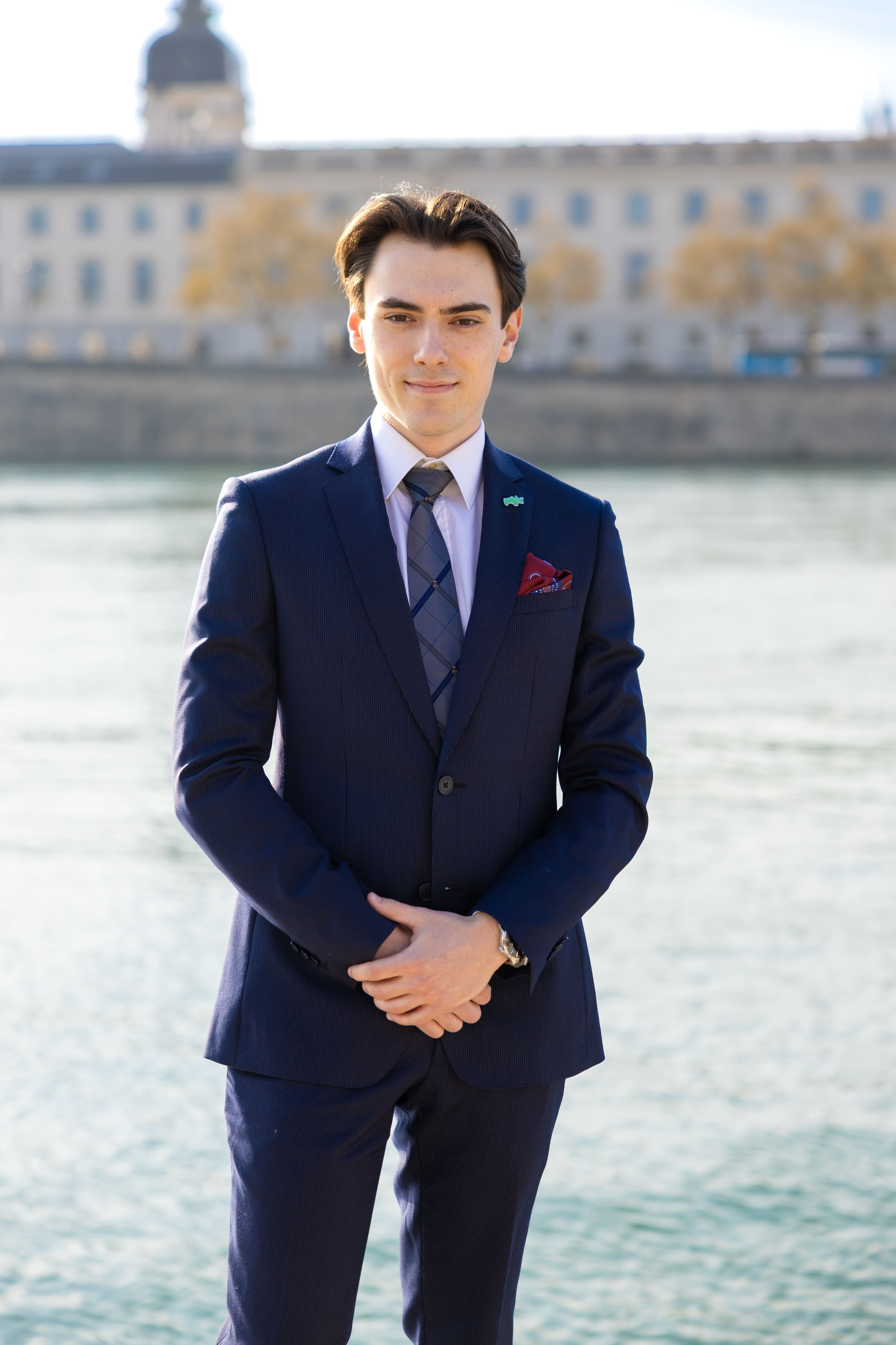Confident young woman in a navy pinstripe suit standing with arms crossed by a riverside with a cityscape background.