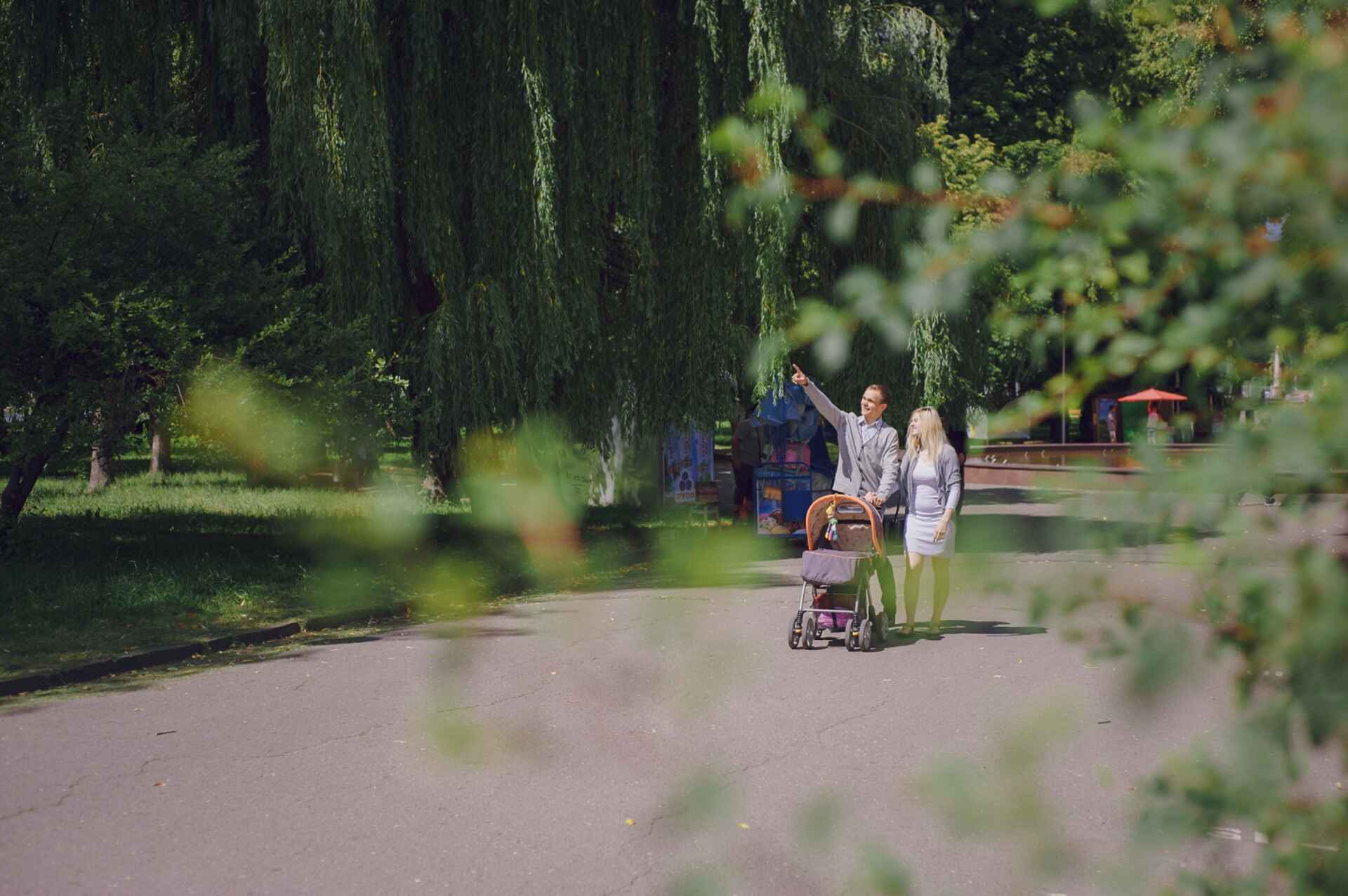 Parent pushing stroller under willow trees in a peaceful park