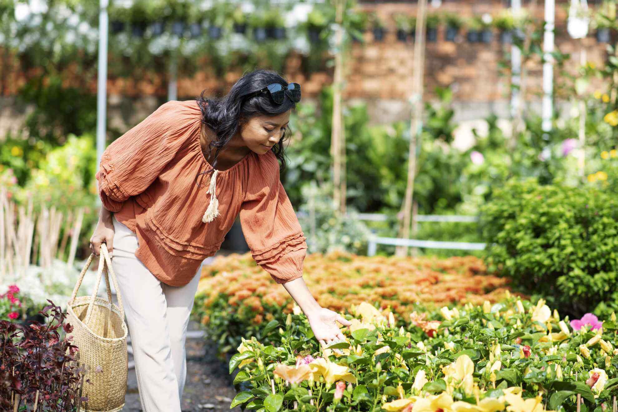 Woman in orange top tending to yellow flowers in a lush garden