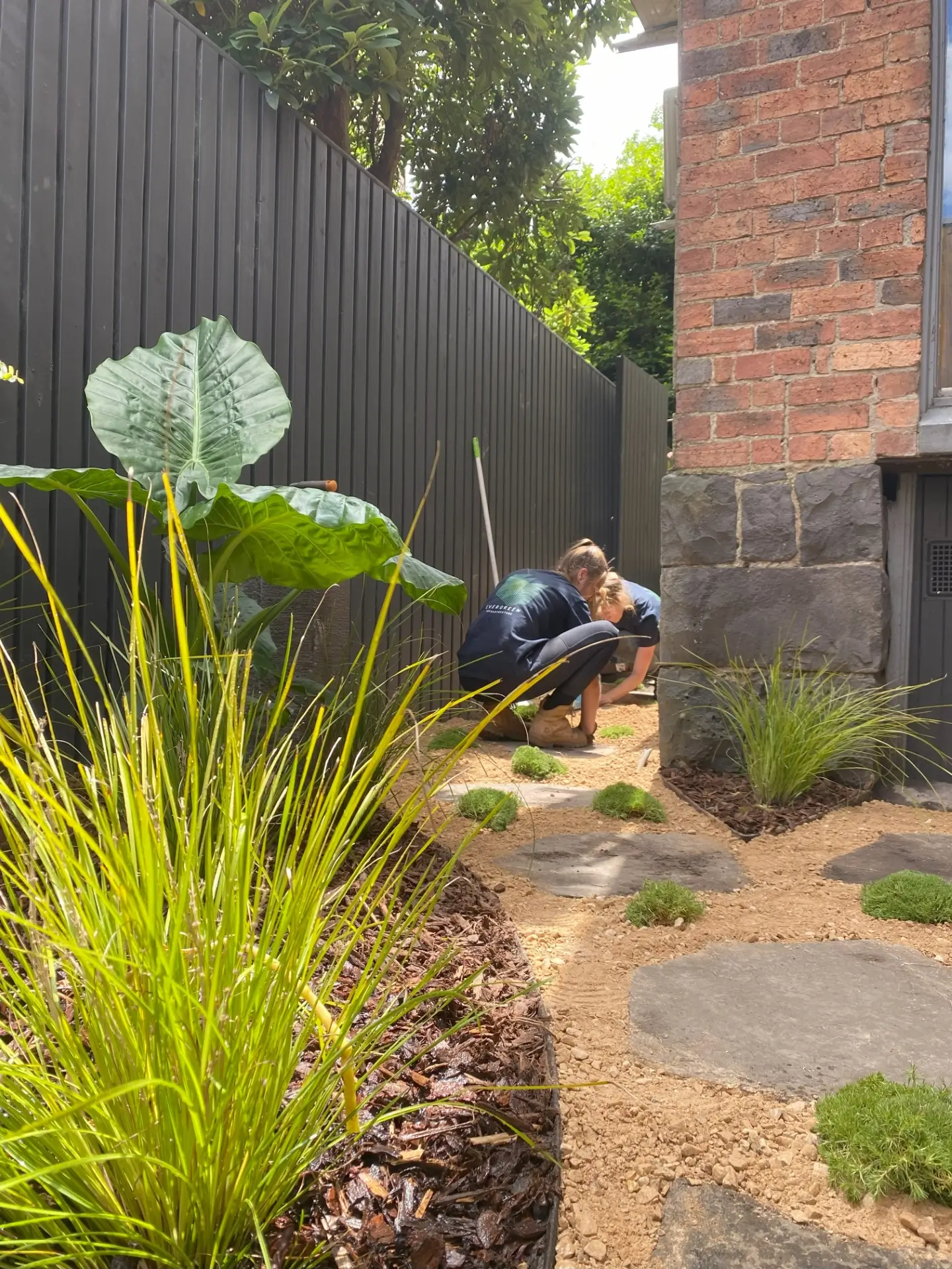 Garden landscaping with ornamental grasses, stone path, and worker planting