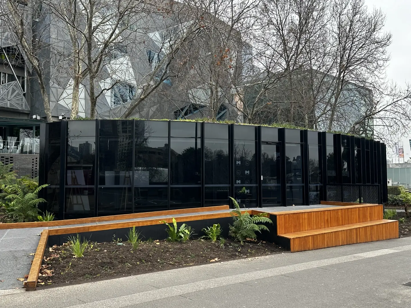 Modern urban landscape with black glass structure, wooden benches, and ferns