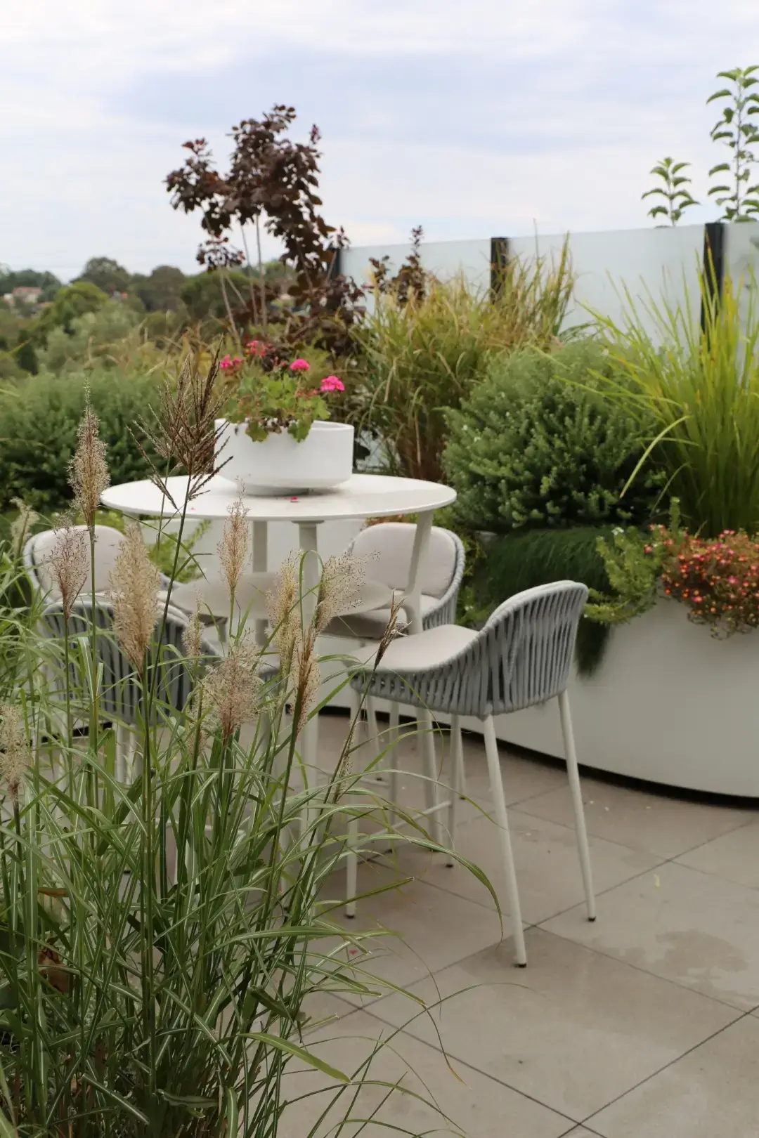 Rooftop garden with white furniture, ornamental grasses, and pink flowers