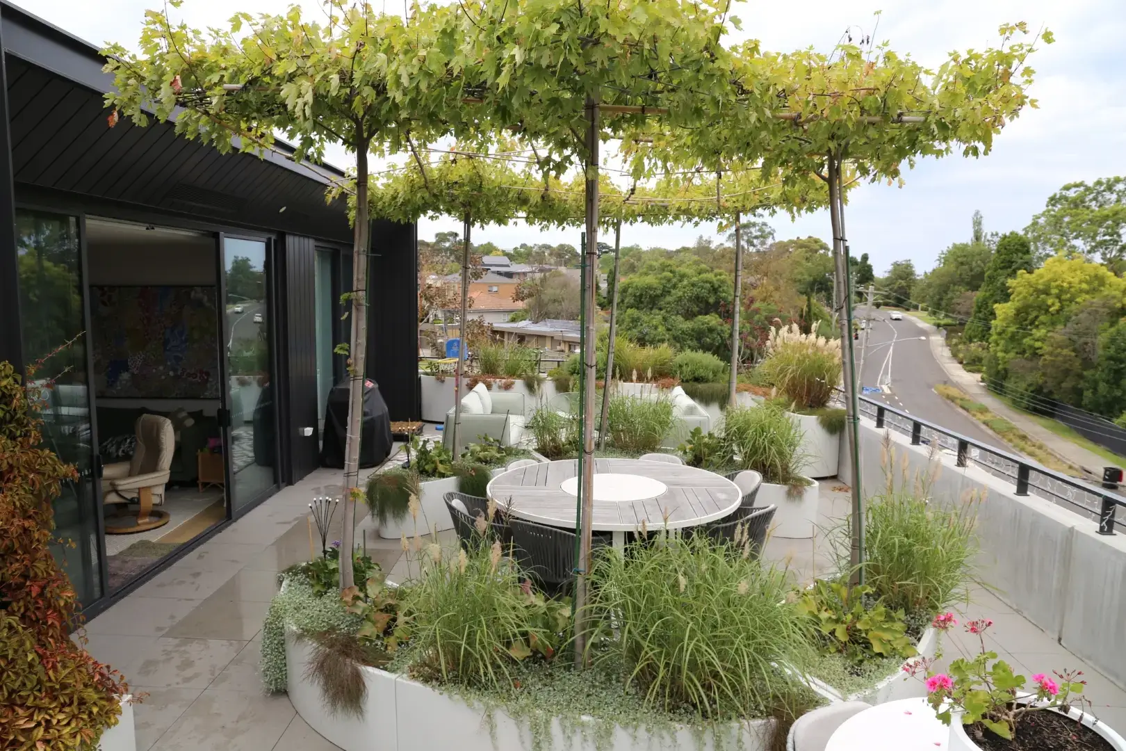 Modern balcony with white planters, dining table, and lush green pergola