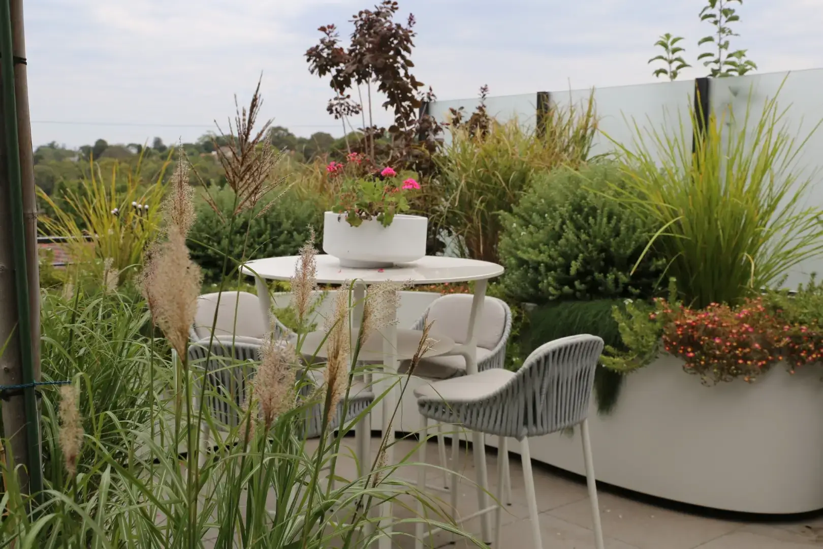 Cozy rooftop garden with white furniture, ornamental grasses, and flowering plants