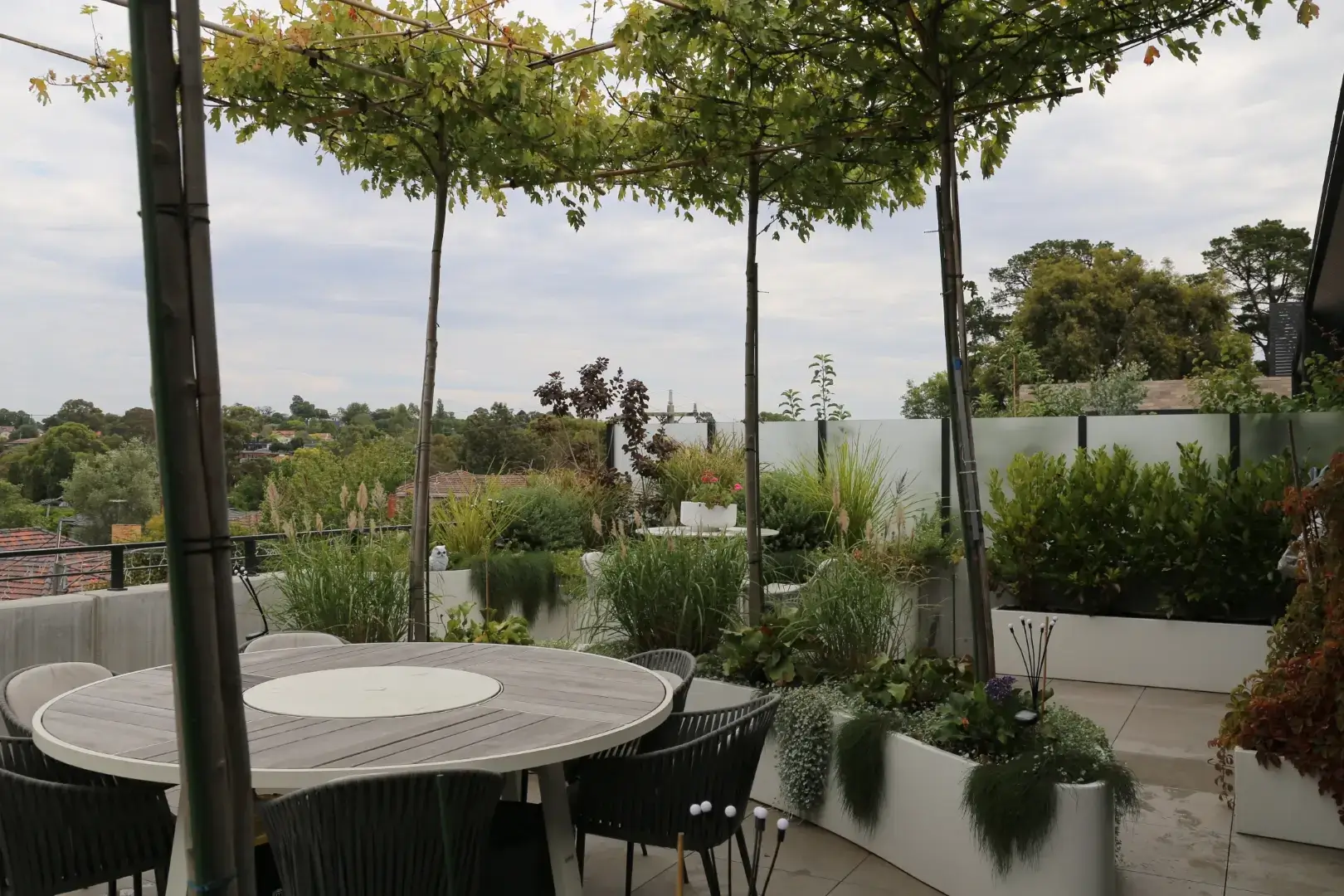 Modern rooftop garden with dining table, planters, and lush greenery