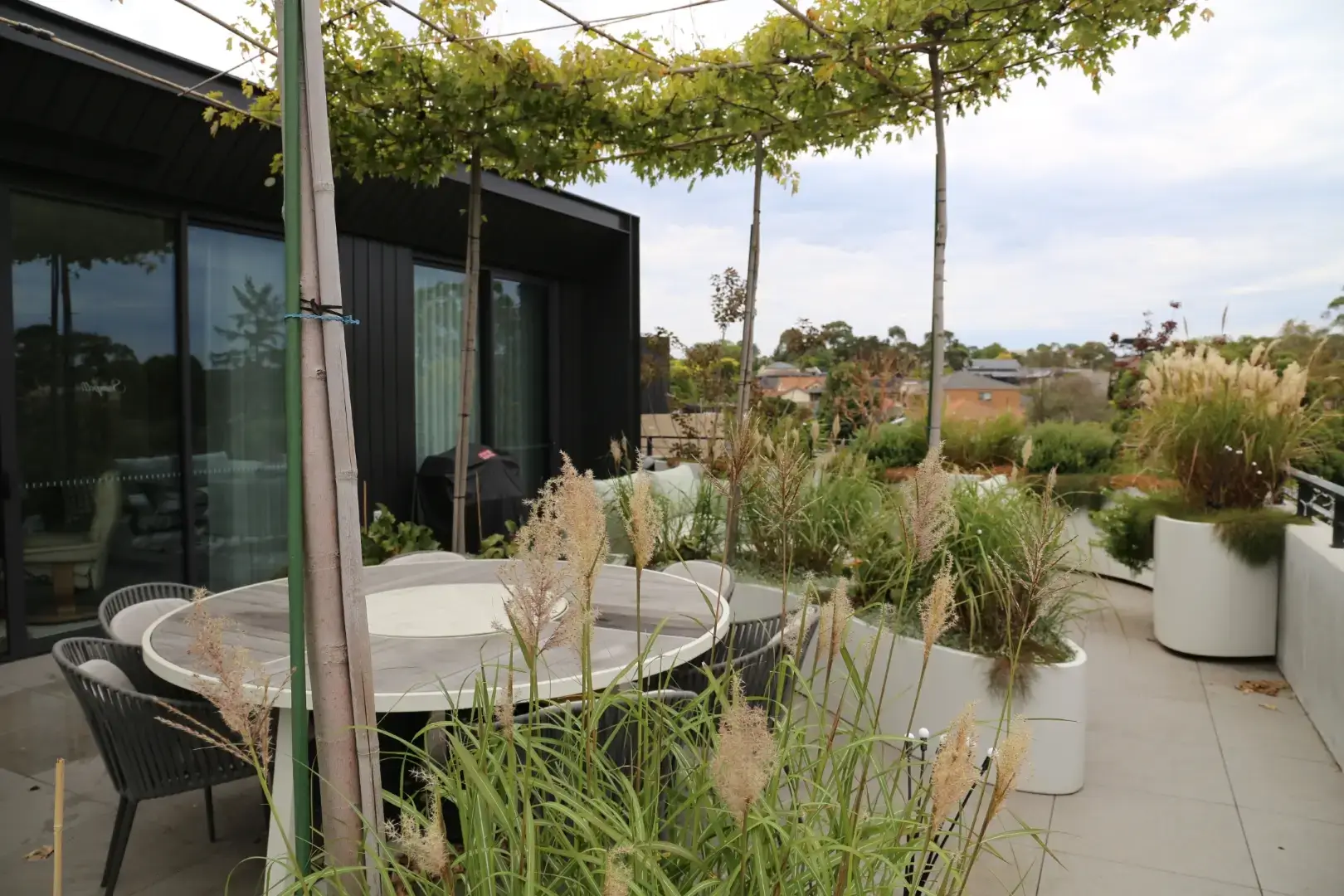 Modern rooftop terrace with dining area, potted grasses, and urban landscape view