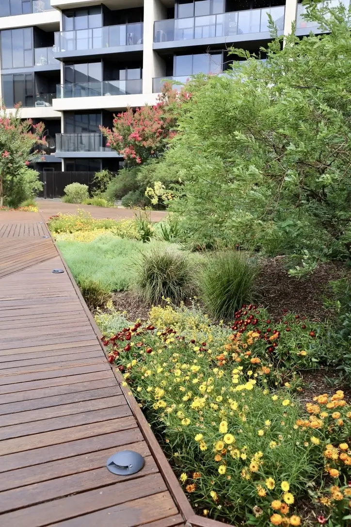 Modern apartment building with wooden walkway and colorful garden landscaping