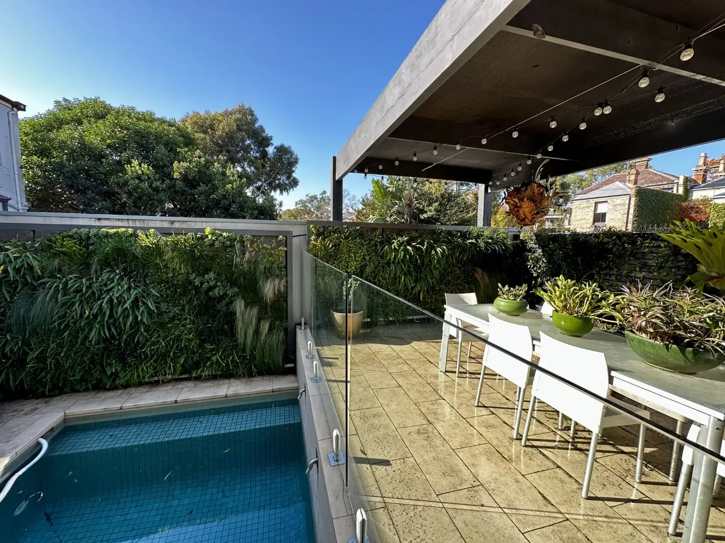 Modern rooftop terrace with pool, dining area, and lush green vertical garden