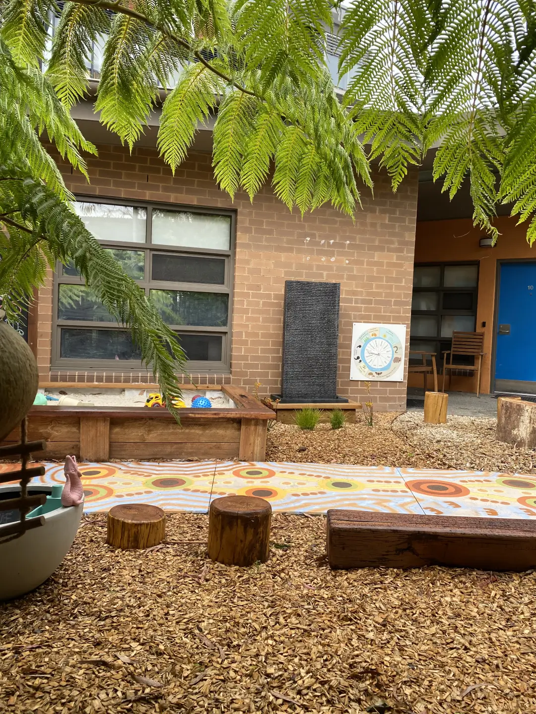Outdoor learning space with ferns, wooden stumps, and decorative tiles