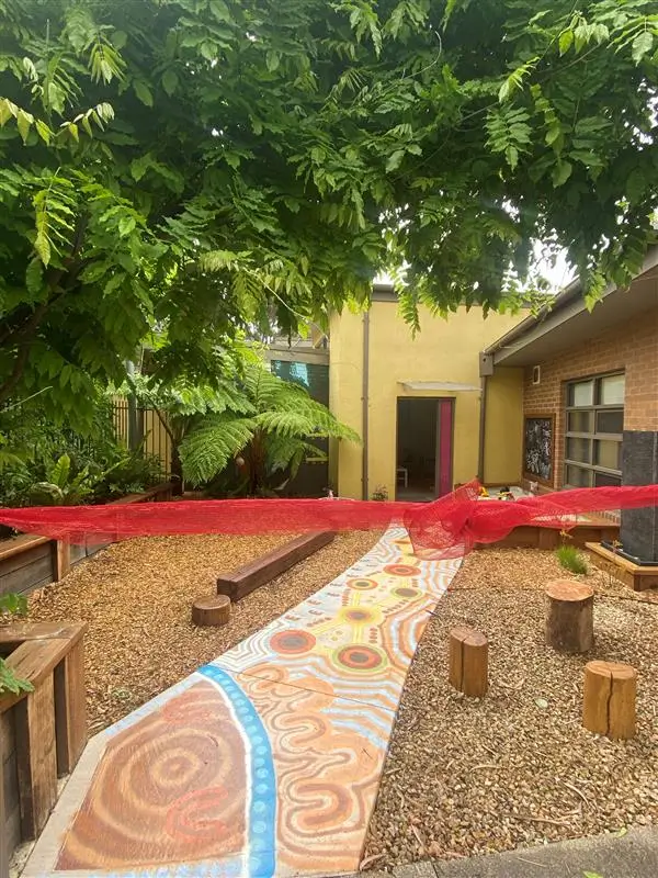 Outdoor yard with colorful painted pathway, wooden logs, and red canopy