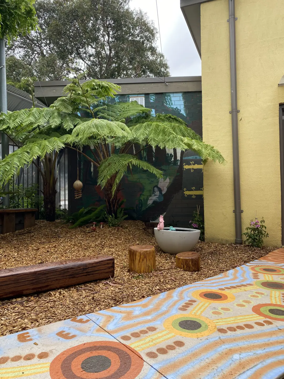 Tree ferns in courtyard with colorful patterned tiles and wooden stools