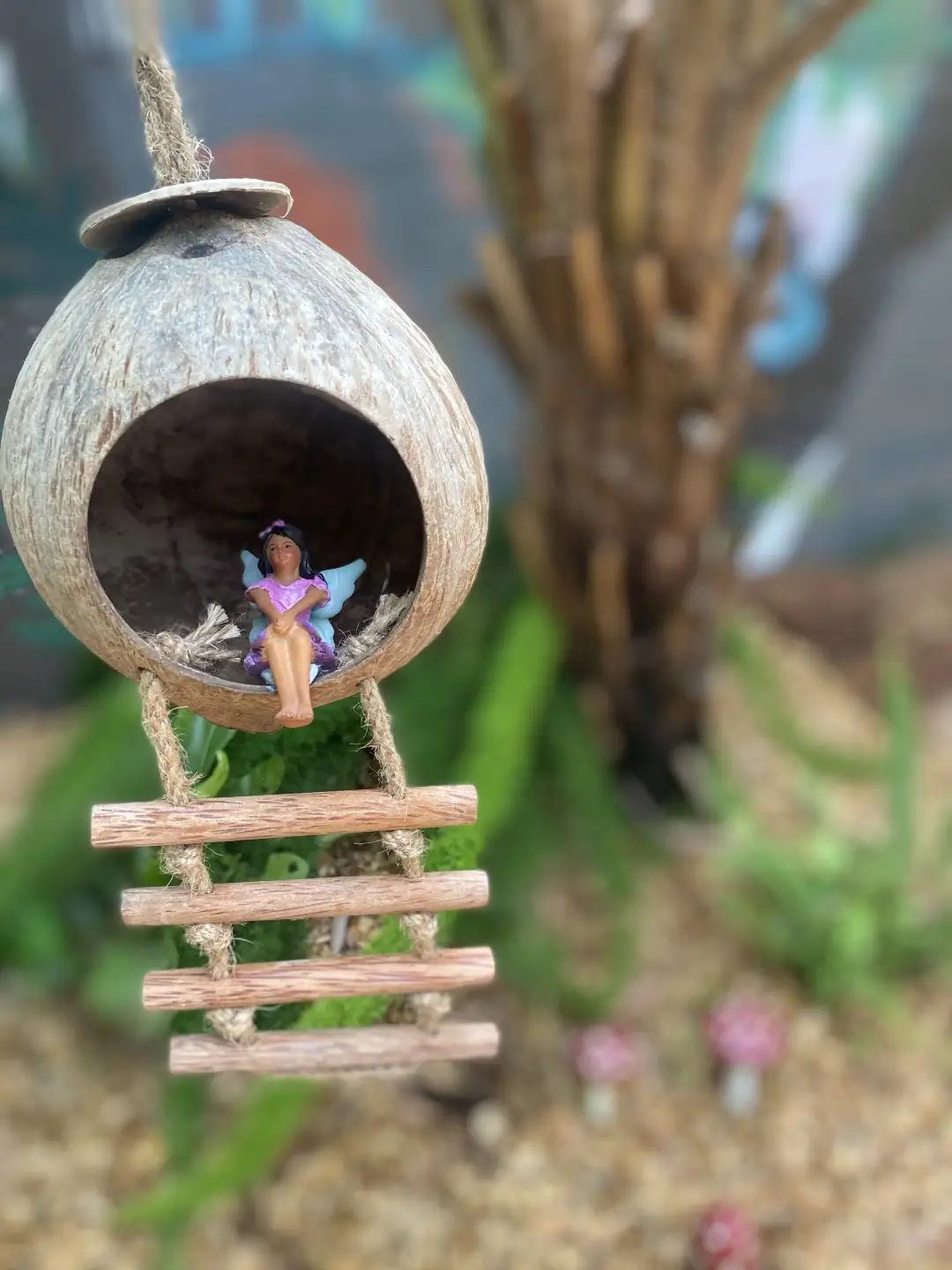 Fairy figurine sitting inside coconut shell birdhouse with wooden ladder