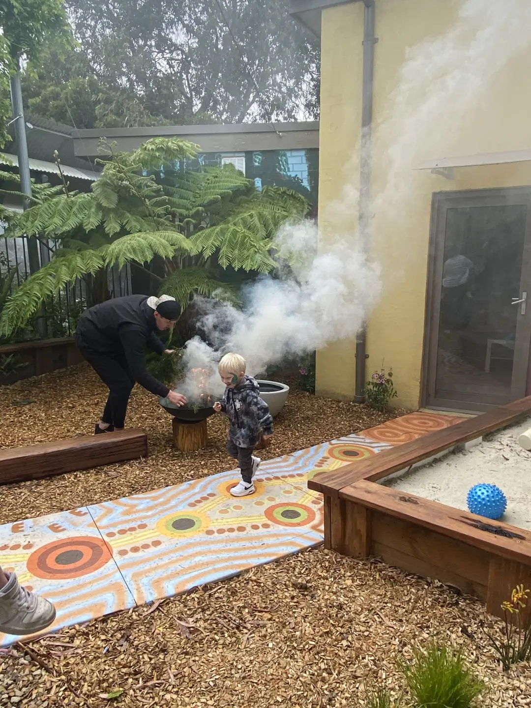 Adult and child explore smoking fire pit in backyard garden
