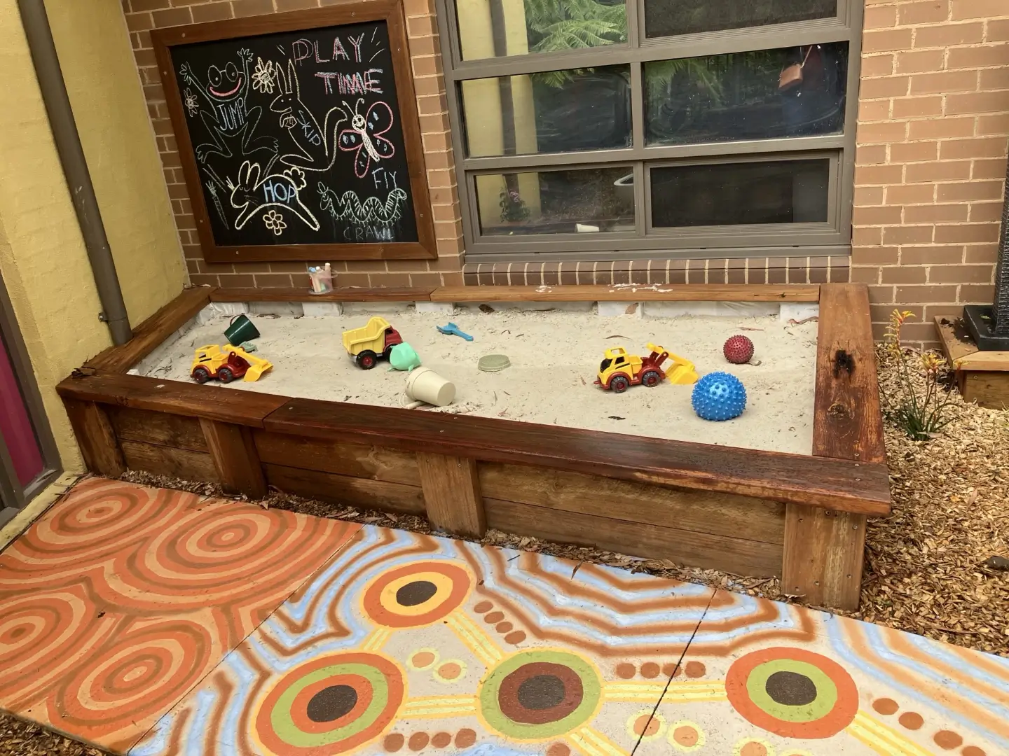 Colorful sandbox with toys, chalkboard, and patterned floor in playful setting