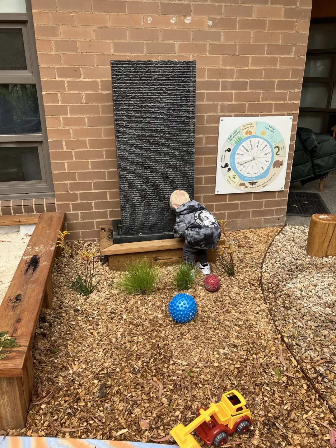 Child examining water feature near seasonal calendar in outdoor play area
