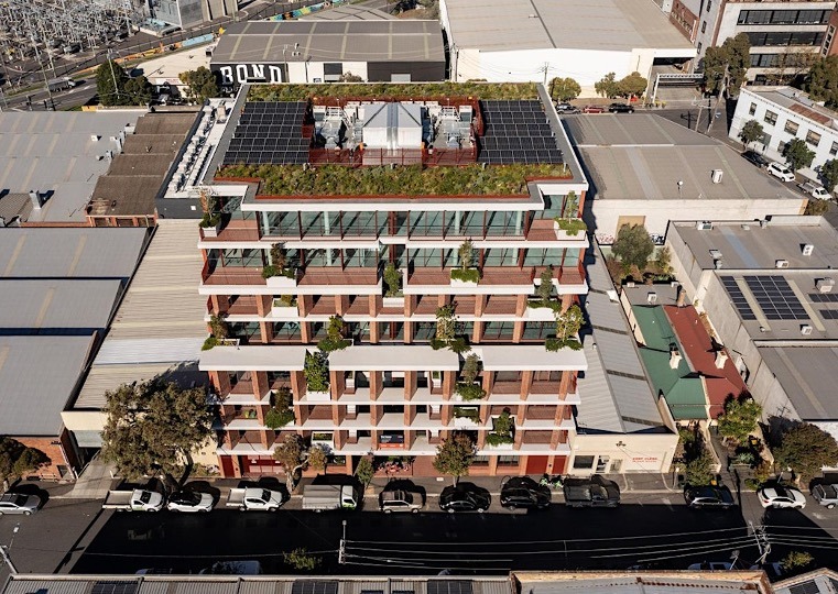 Aerial view of an apartment building with a green roof, balcony planting on every level, and rooftop solar panels