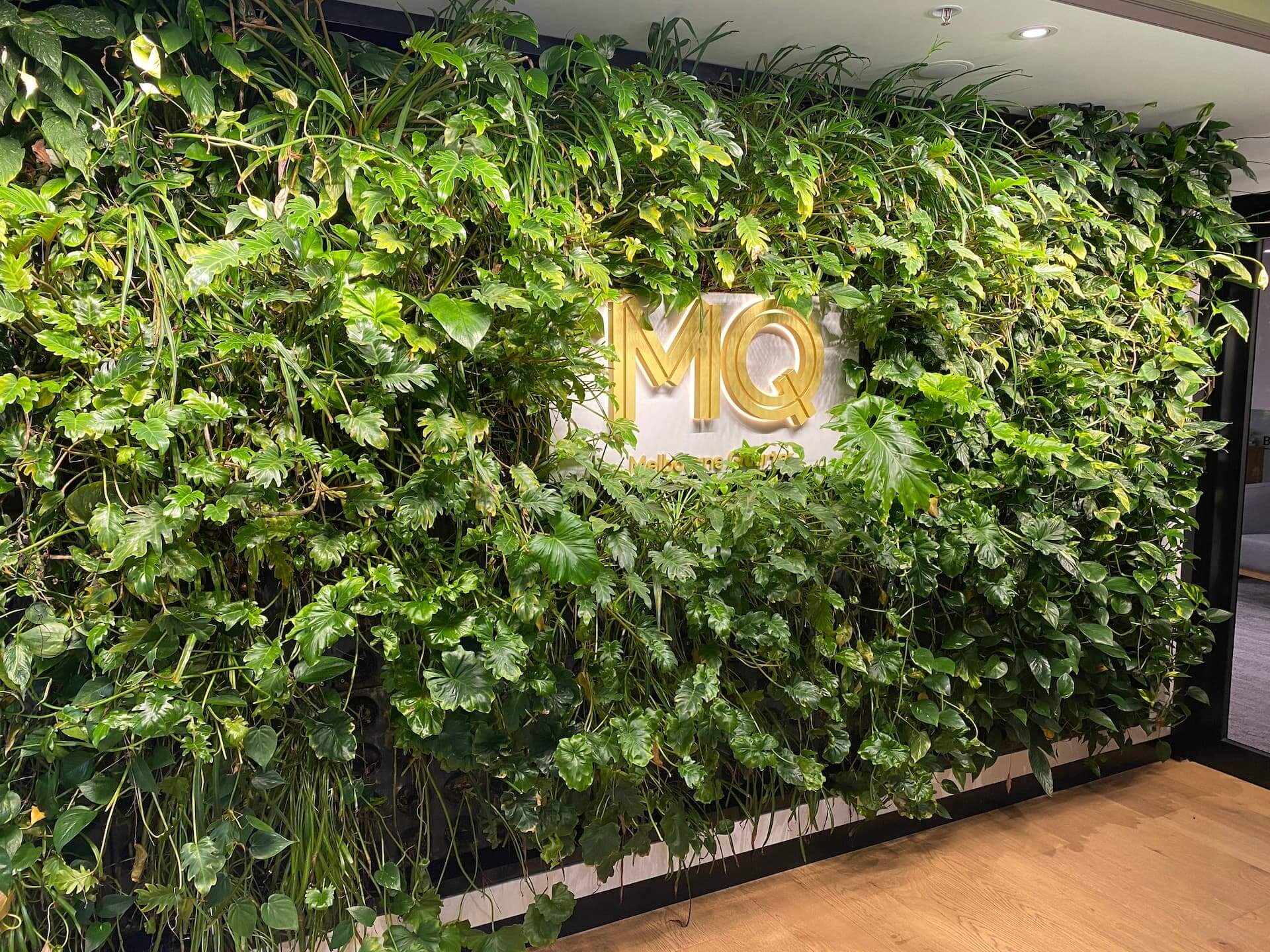 A lush indoor living green wall covered in a dense variety of tropical foliage plants, framing a gold, a striking example of nature-based solutions applied to interior commercial architecture.