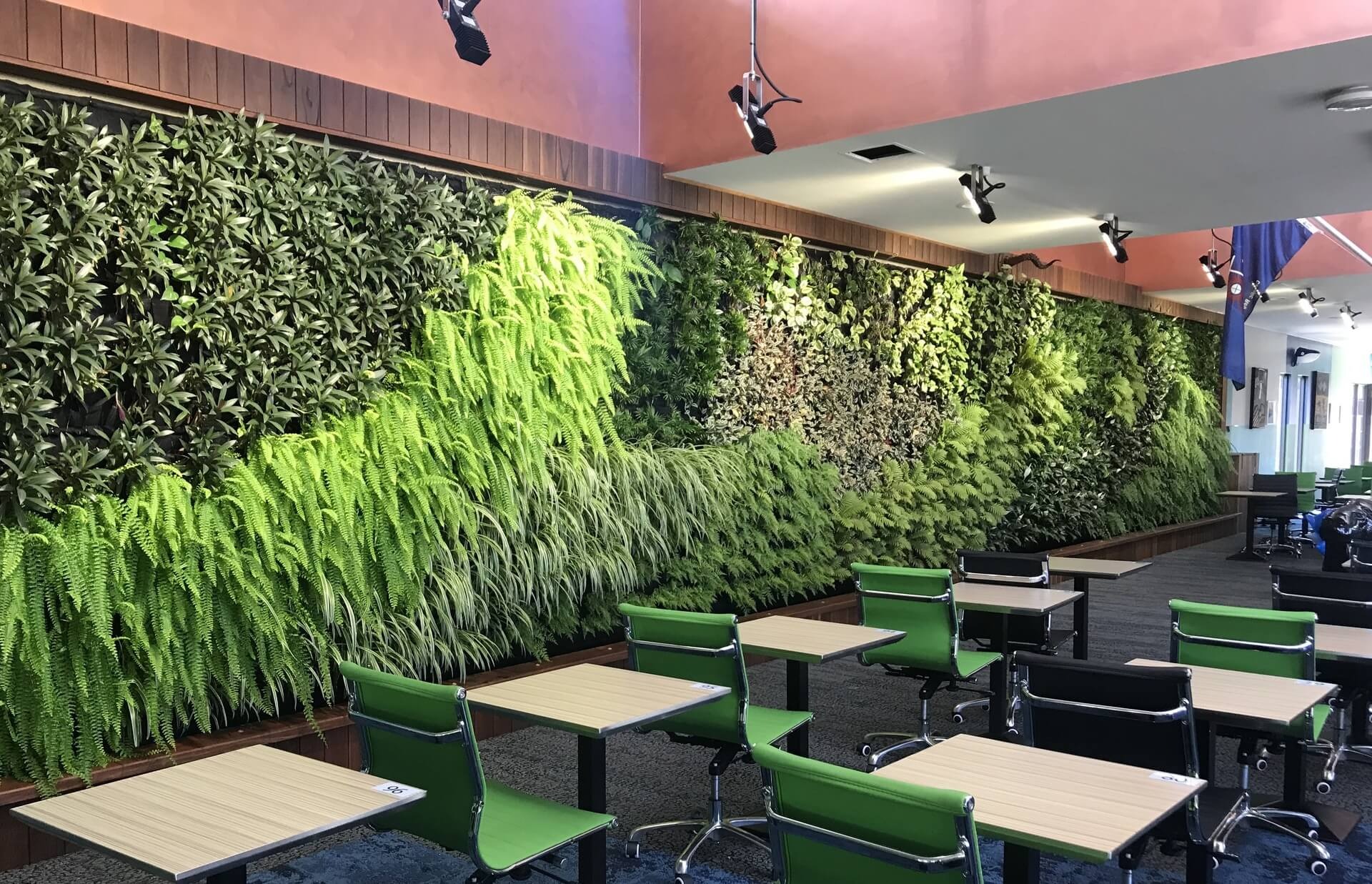Lush green living wall with ferns and trailing plants behind a café dining area.
