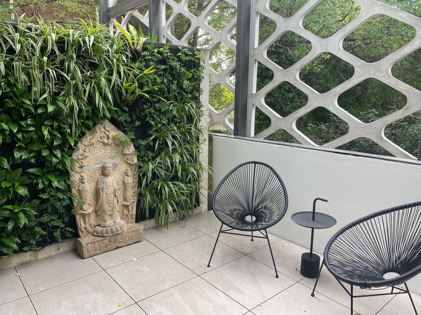 Outdoor living wall of spider plants and greenery beside a stone Buddha statue on a patio.