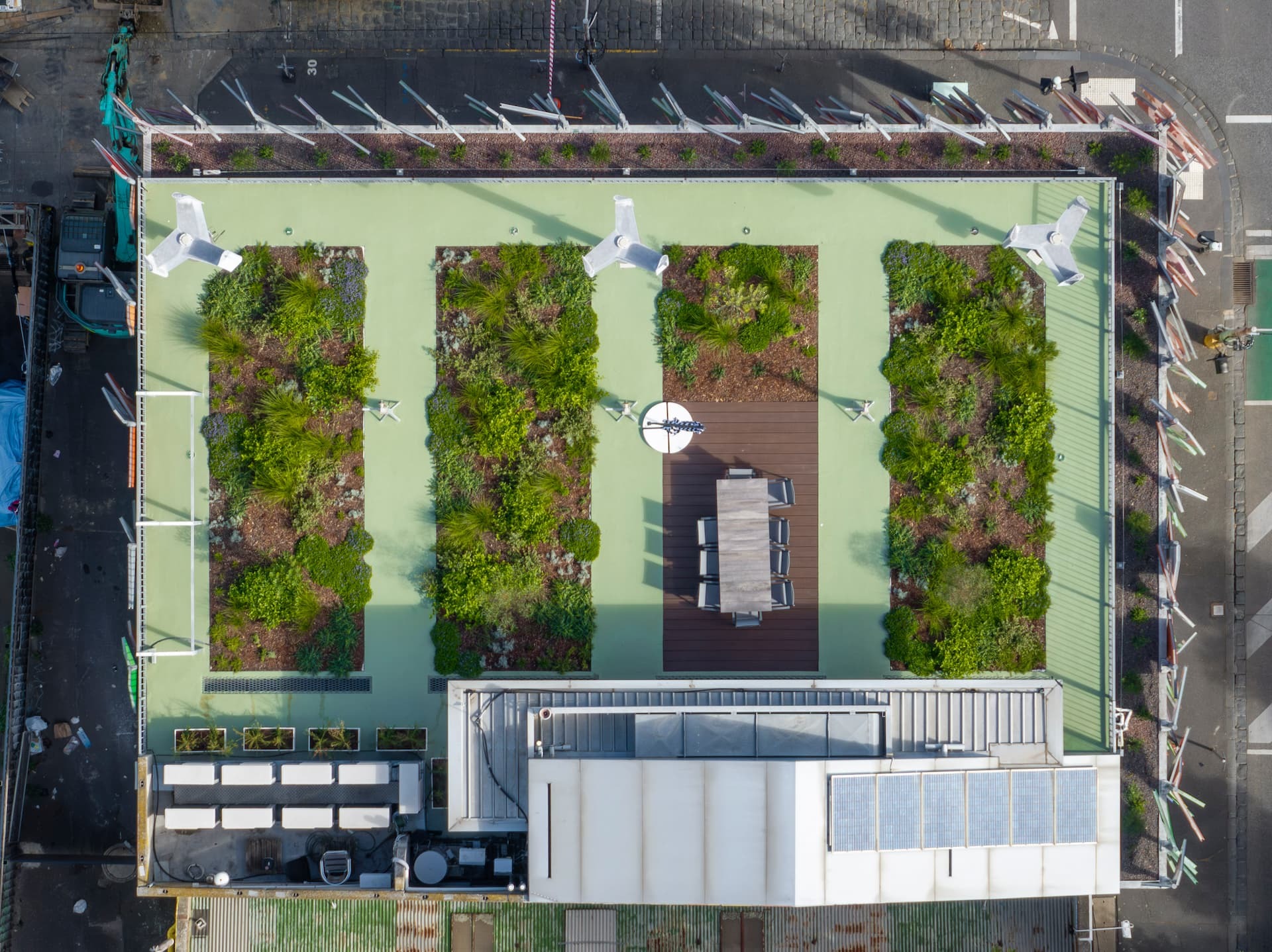 Aerial view of a green roof with four planted beds, a timber dining terrace and solar panels above a city street.