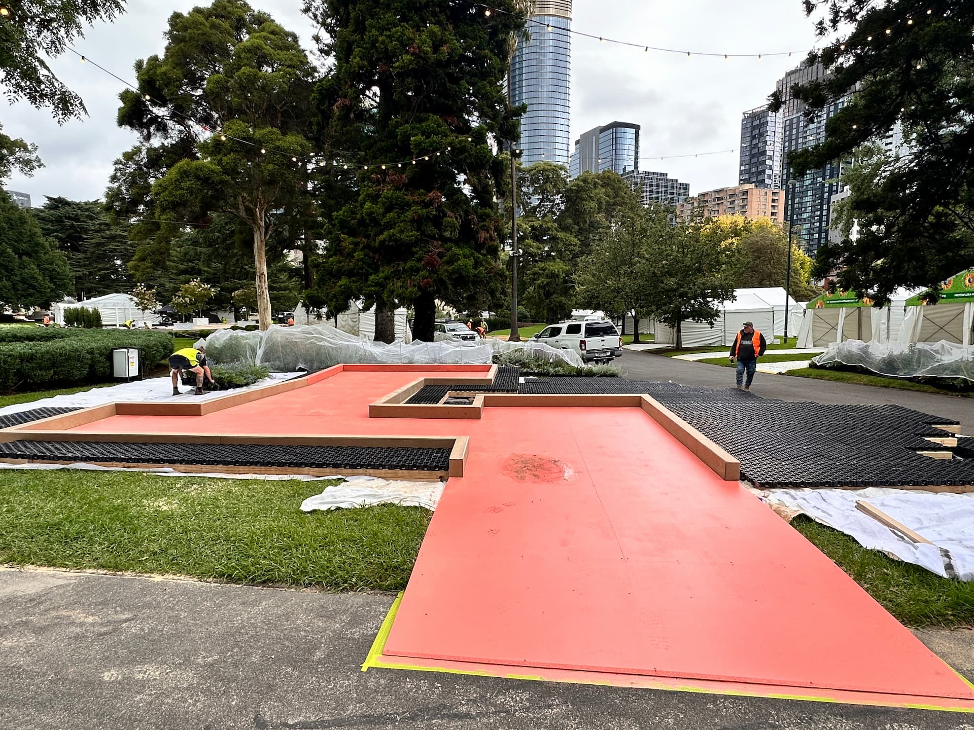 Raised timber deck painted red with grass matting underlay, part of the Plant Futures display construction in Melbourne.