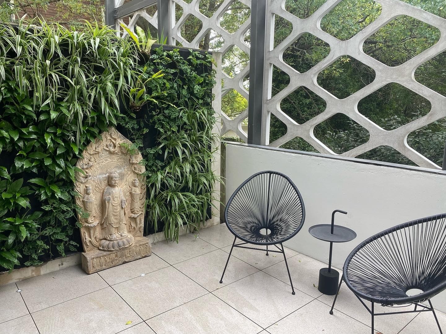 Outdoor terrace living wall with ferns and spider plants beside seating and a stone Buddha statue