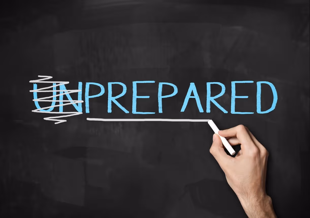 A hand holding chalk writing the word "unprepared" on a blackboard, with the "un" being crossed out, leaving the word "prepared.