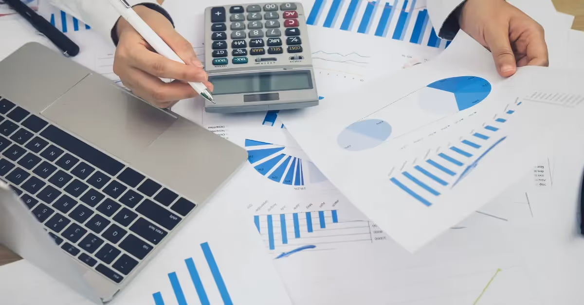 close-up of an accountants hands working with a laptop, calculator, and printed reports