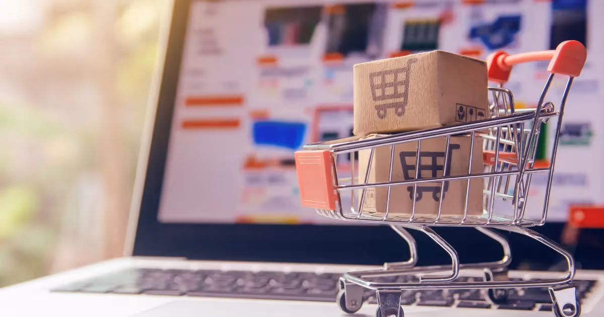 a laptop with an ecommerce website on the screen and a graphic of a shopping cart with shipping boxes inside of it