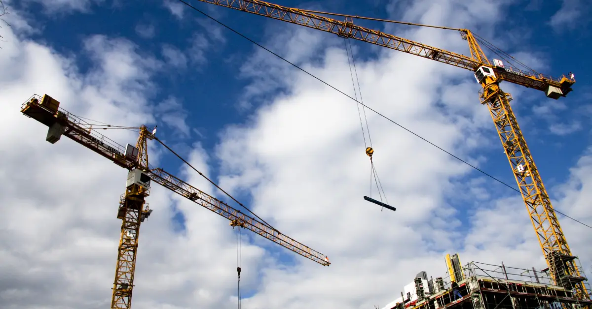 Two tower cranes lift materials over a building site, representing construction in progress on a large capital project