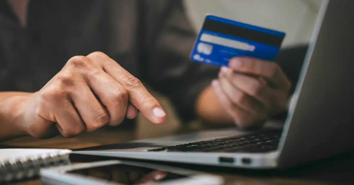 Person holding a company credit card while typing on a laptop