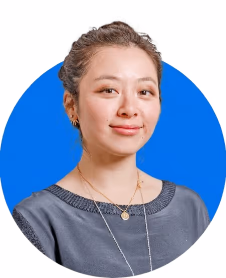 Portrait of a woman with light makeup and a subtle smile, wearing a gray top and gold necklaces, against a blue circular background.