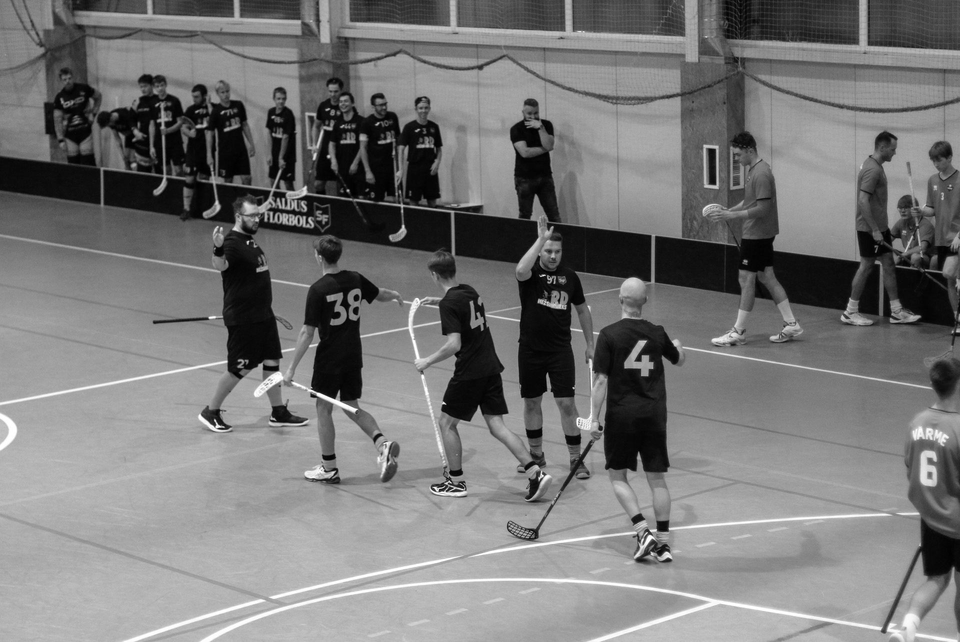 Florbola spēlētāji sporta laukumā, atzīmējot vārtus vai uzvaru ar roku pacelšanu.