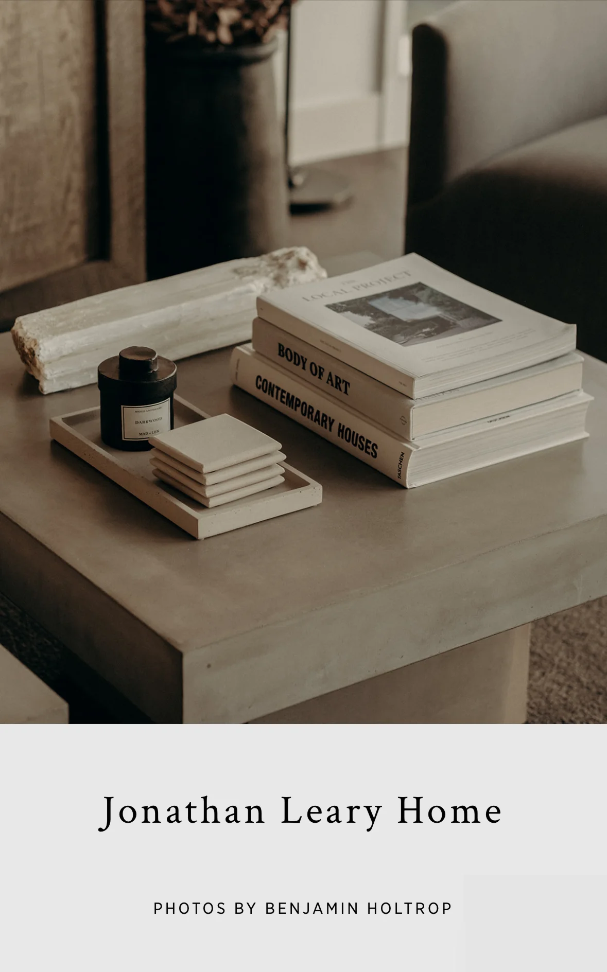 Stylish flat-lay of a home interior detail featuring stacked design books, a candle, and ceramic coasters on a wooden surface. 