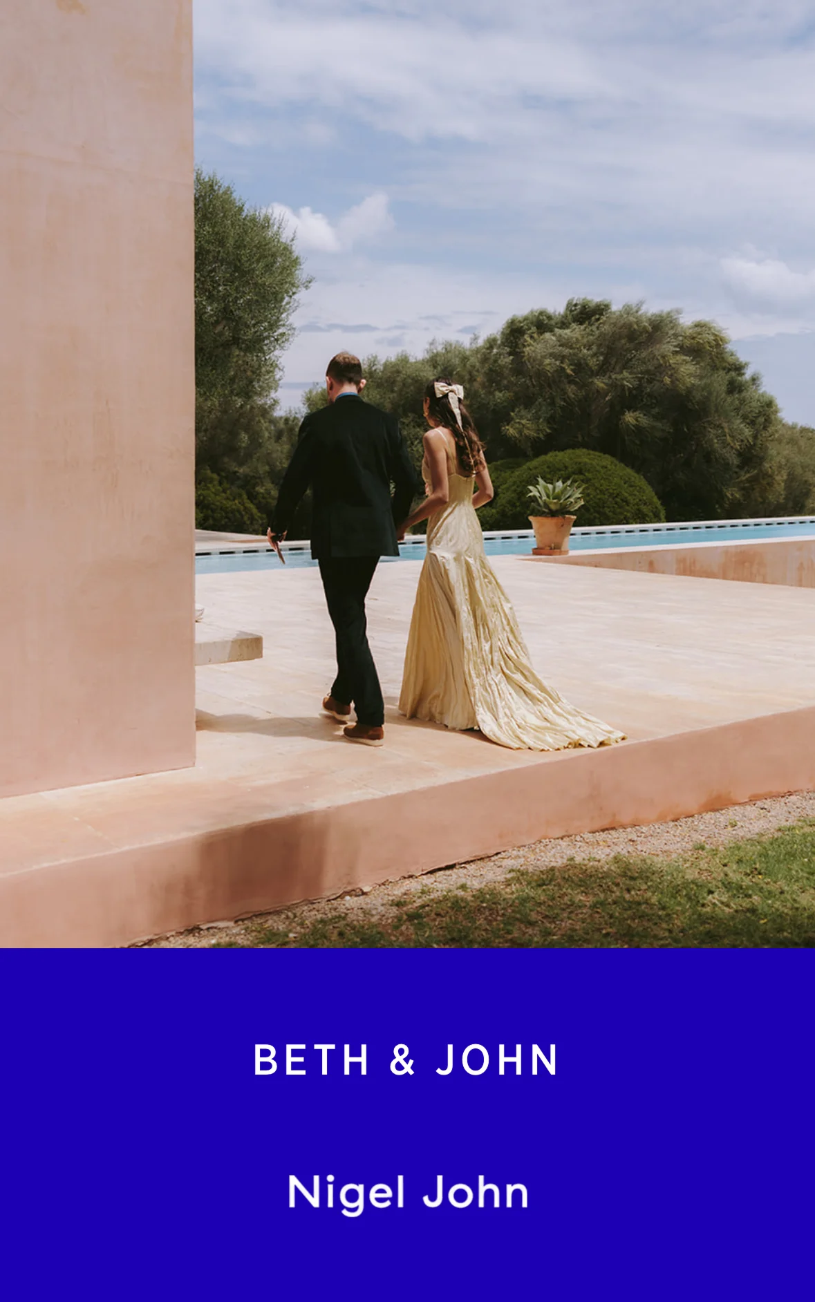 Elegant outdoor wedding moment with a couple holding hands near a reflective pool and modern architectural structure under a blue sky. Photo by Nigel John