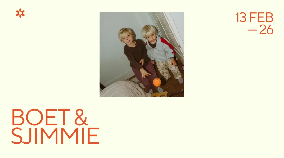 Two young boys, one in a brown top and the other in a light jacket with red stripes, stand indoors looking up with an orange ball in mid-air between them.