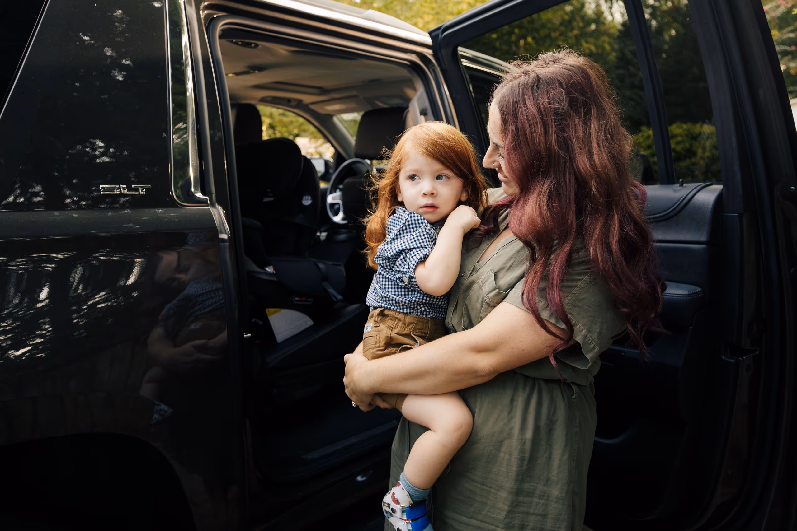 Woman holding a young child beside an open car door.