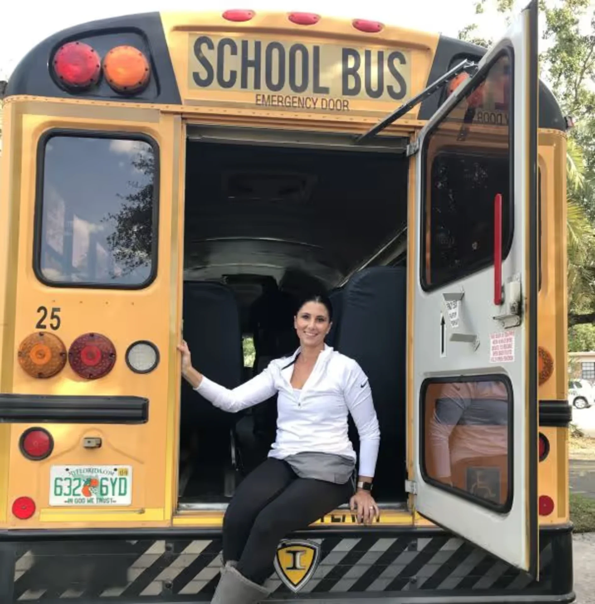 Woman in white jacket sitting in the open emergency door of a yellow school bus with Florida plates.