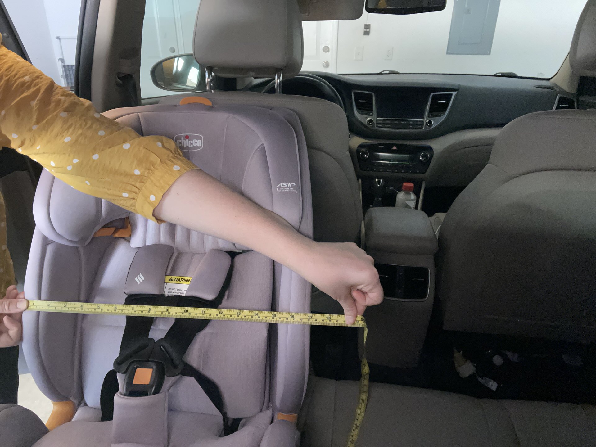 Measuring a car seat with a yellow tape measure to determine width in the backseat