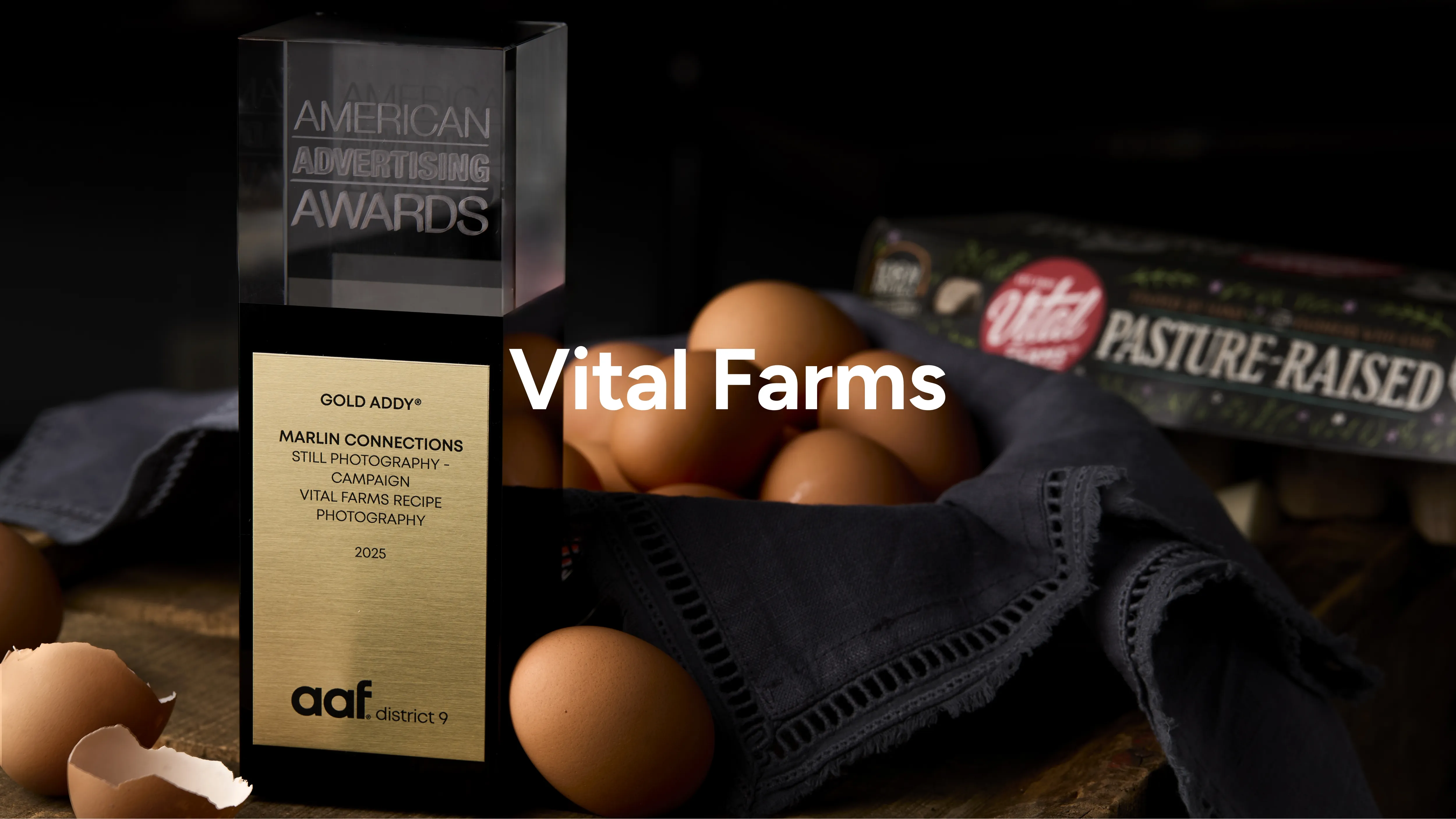 A gold advertising award trophy sits on a dark cloth next to brown eggs, some cracked open, with a Vital Farms pasture-raised egg carton in the blurred background.