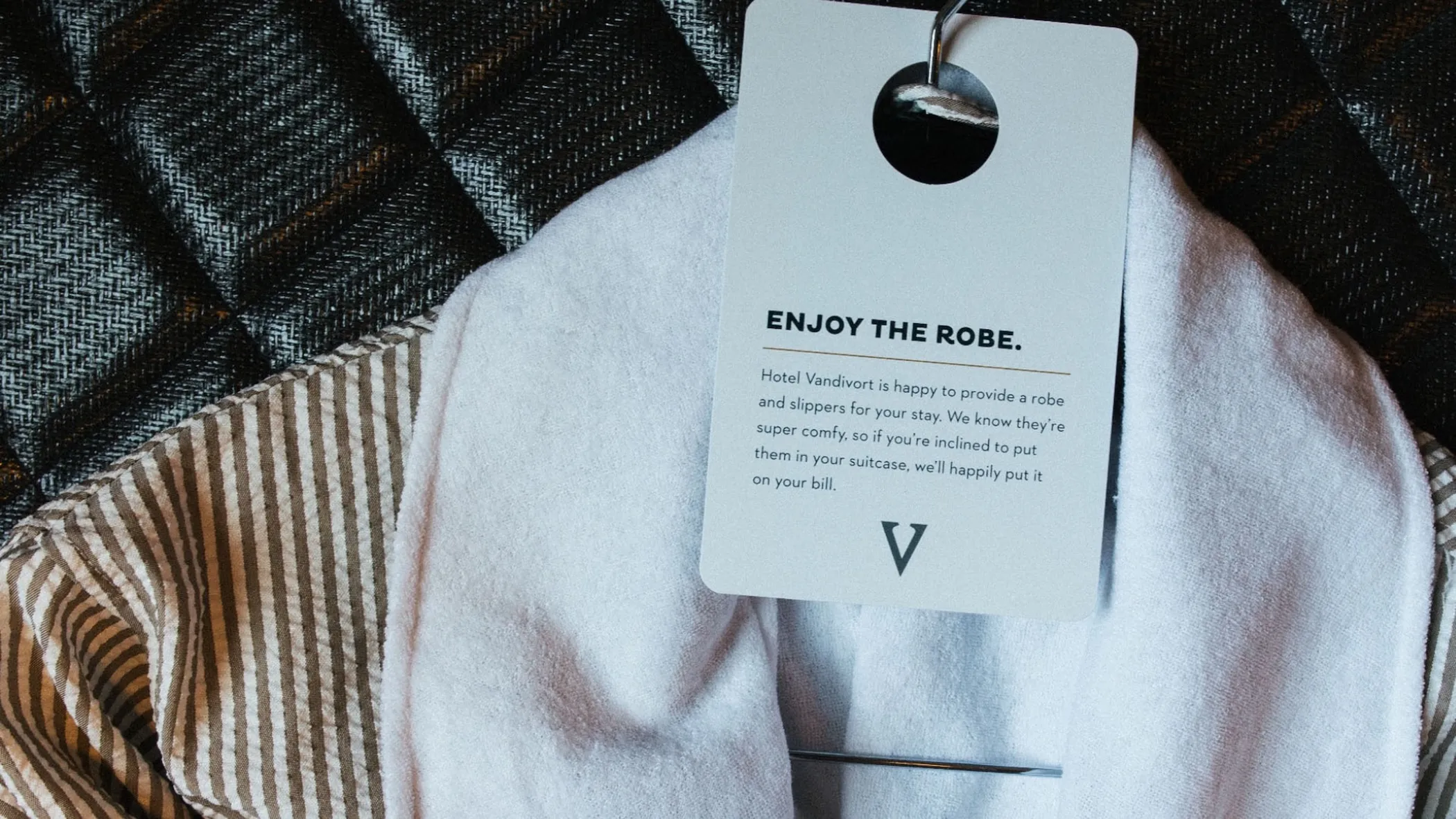 A white hotel robe with a tag that reads Enjoy the Robe, noting that guests may purchase the item if they choose to take it home.