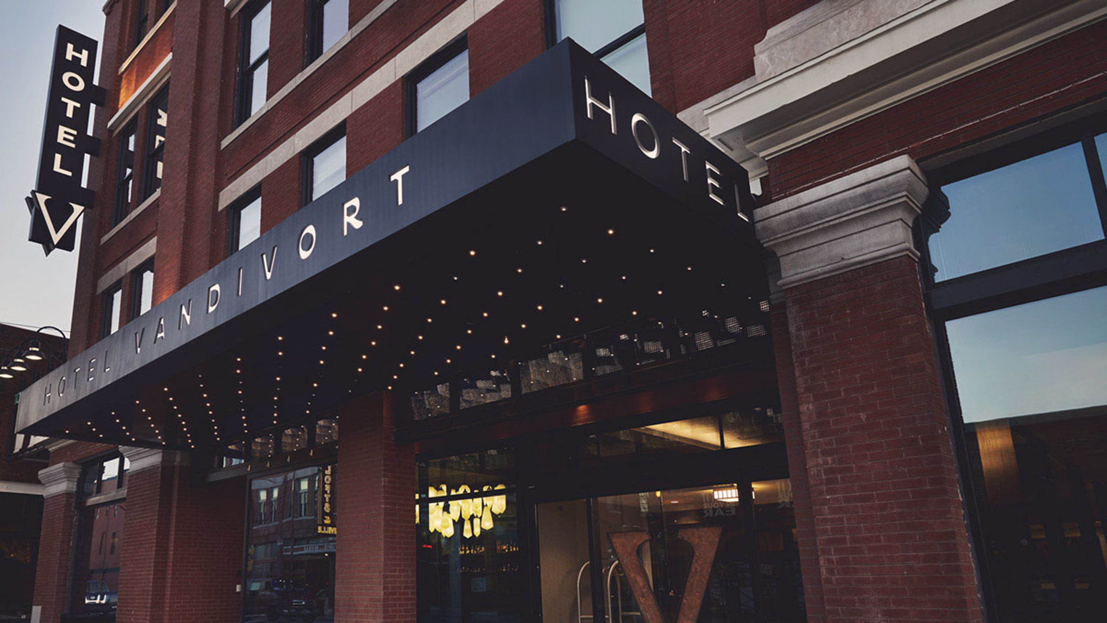 The exterior entrance of Hotel Vandivort, featuring a dark awning with built-in lights and a vertical hotel sign on the red brick building.