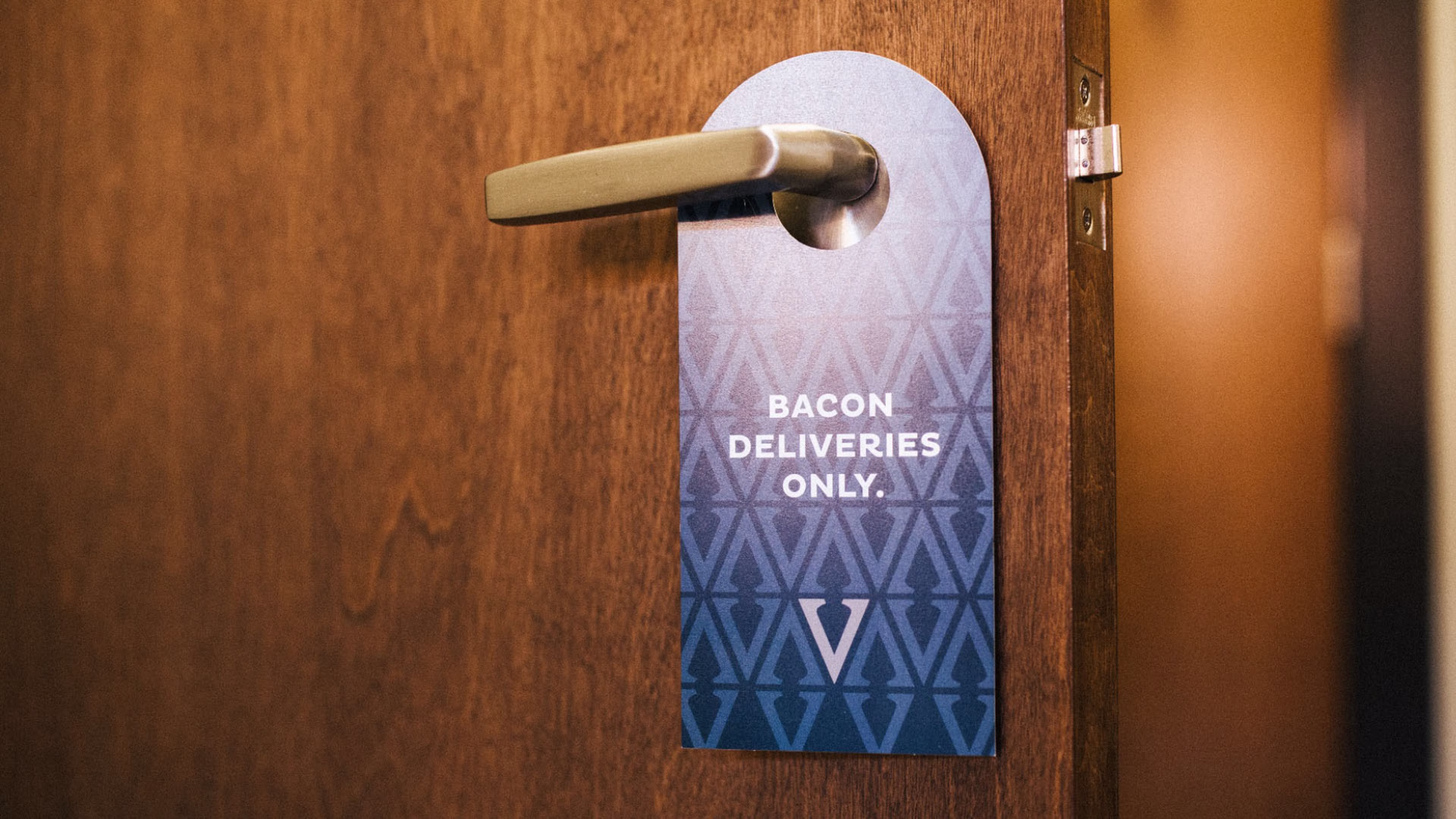 A blue patterned door hanger on a door handle that reads, BACON DELIVERIES ONLY.
