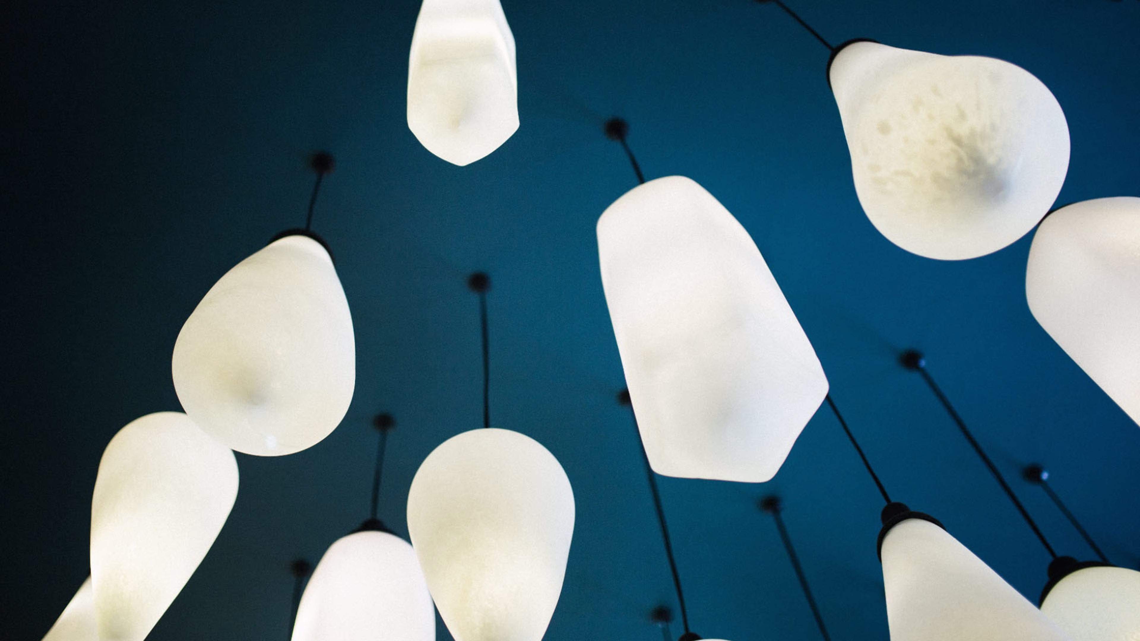 A cluster of white, teardrop-shaped pendant lights hanging against a dark blue ceiling.