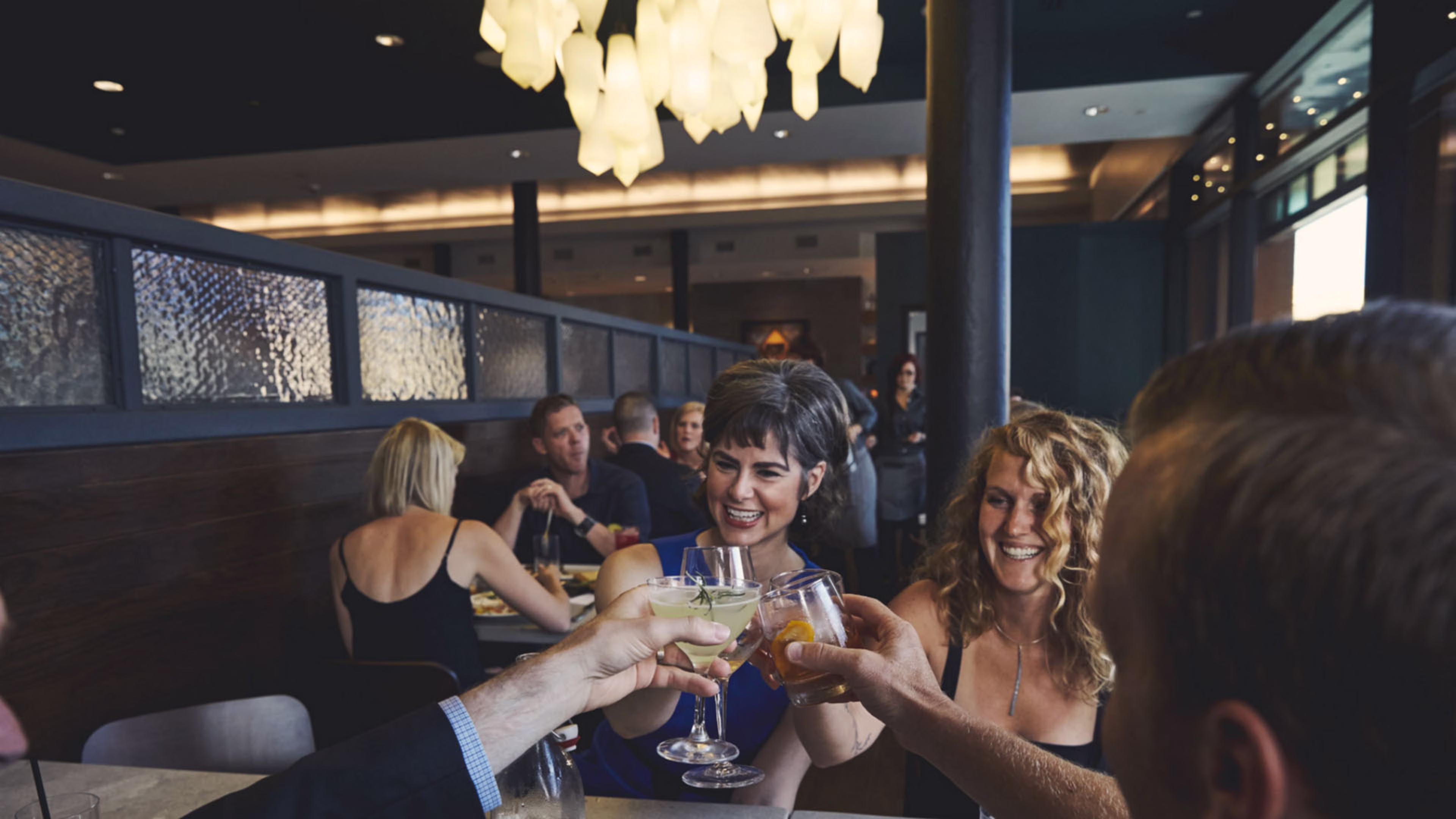 A group of friends at a restaurant clinking glasses filled with cocktails.