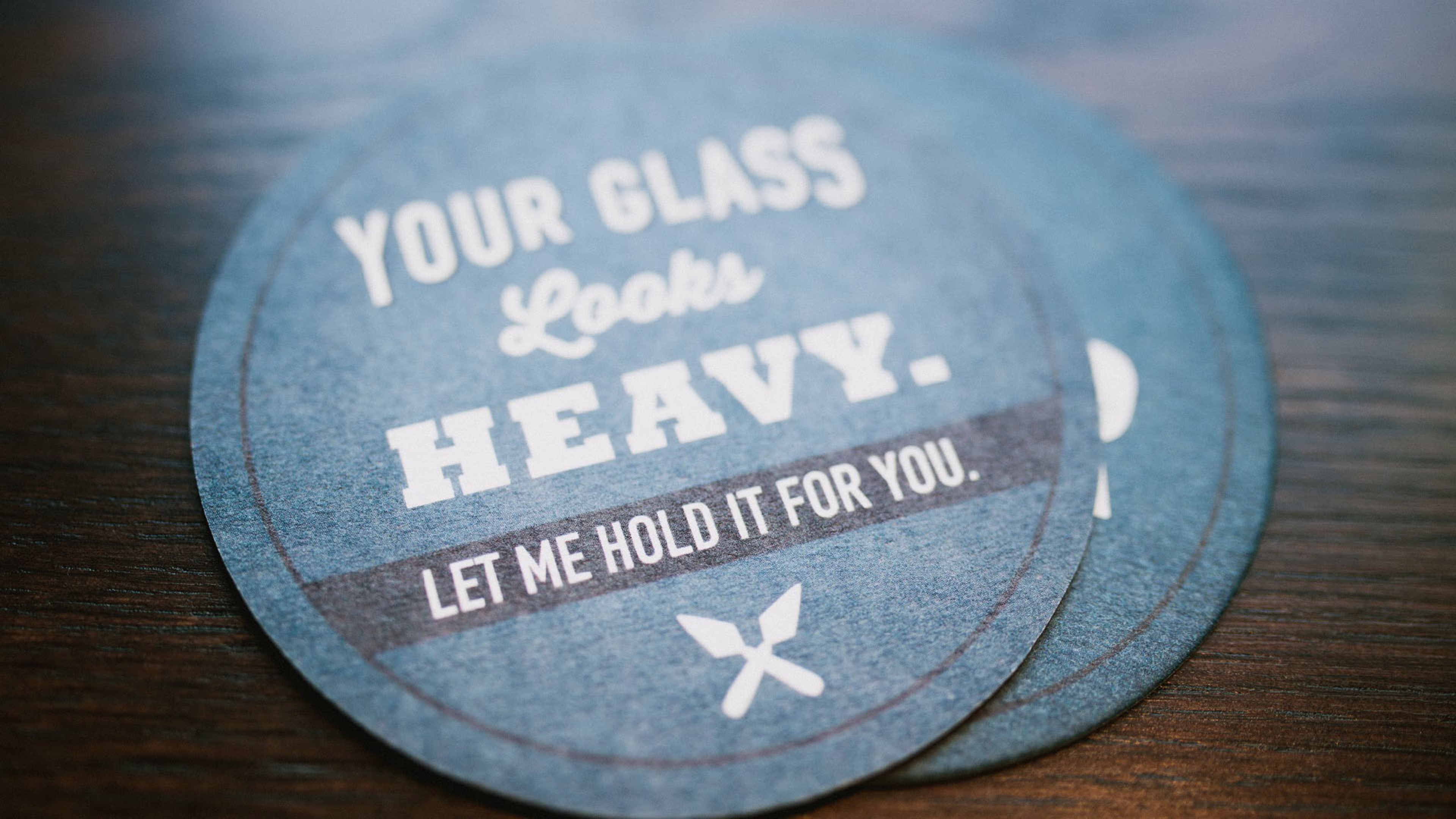 Round blue coaster that reads, YOUR GLASS Looks HEAVY. LET ME HOLD IT FOR YOU.