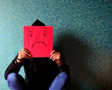 A person sitting in a green room holding up a red card with a sad face drawn on it