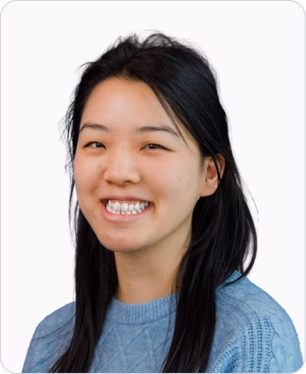 Smiling woman with long black hair wearing a light blue sweater against a white background.